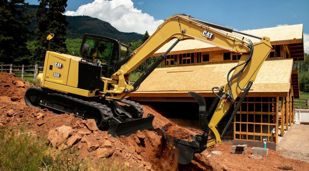 A Caterpillar 308CR mini excavator with long-stick attachment, shown on a construction site.